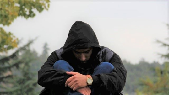 Male with a black hoodie sitting with their head down